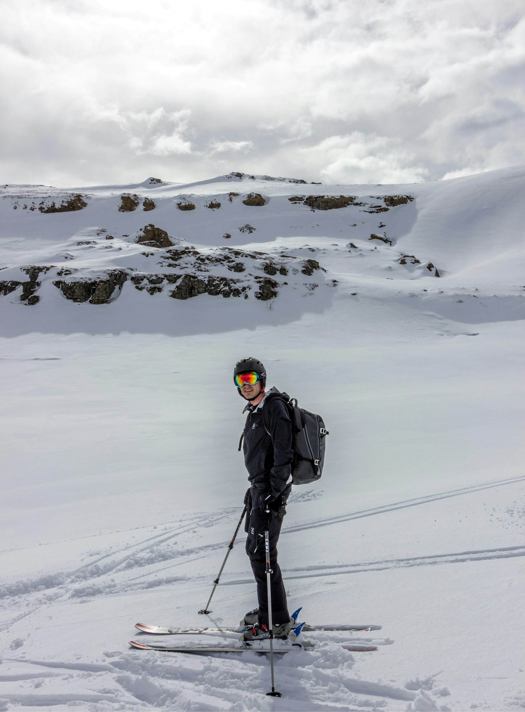 A skier standing on a high ridge scoping a steep line among snowy peaks