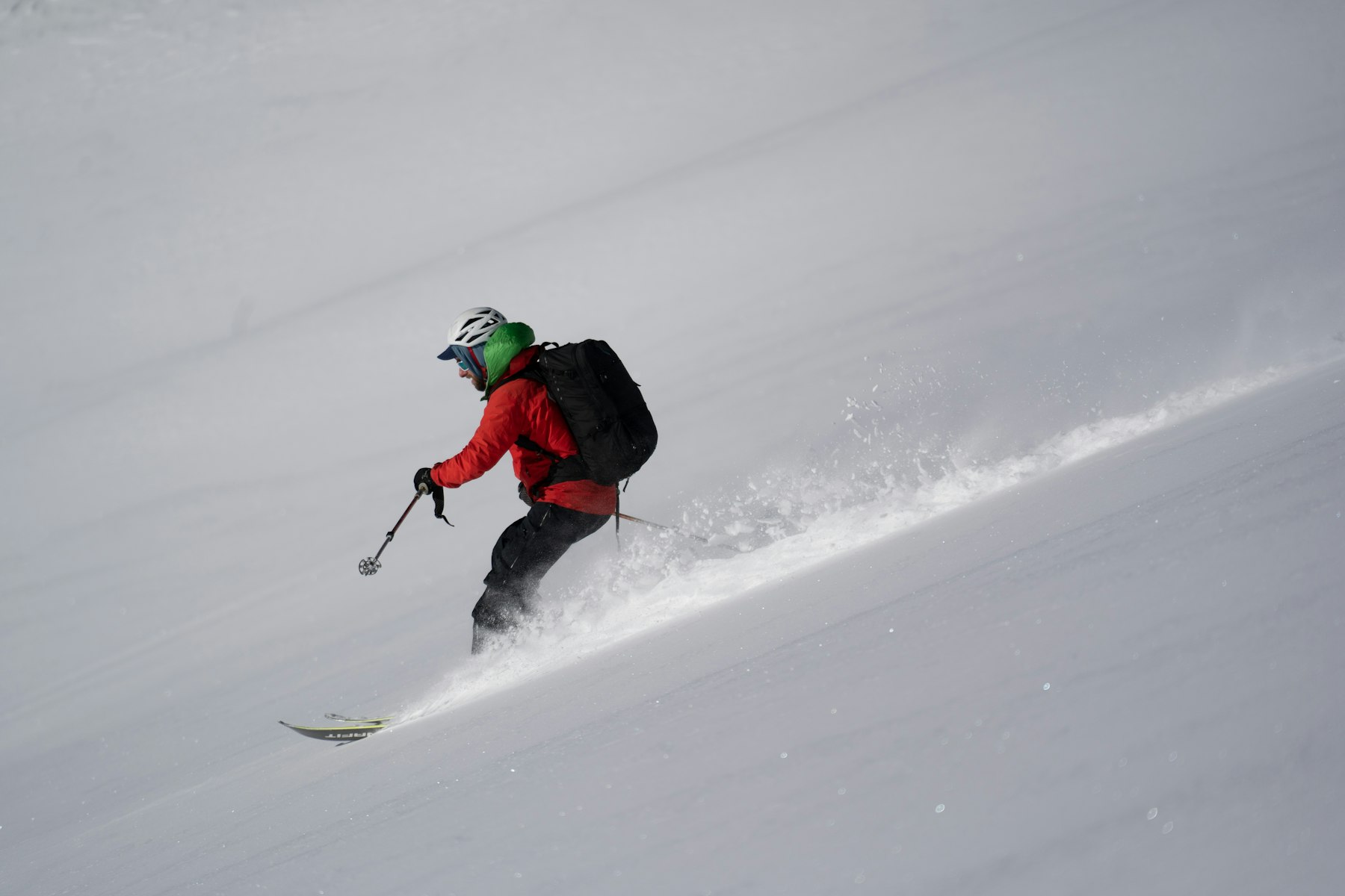 A skier in a red jacket making a turn in deep powder