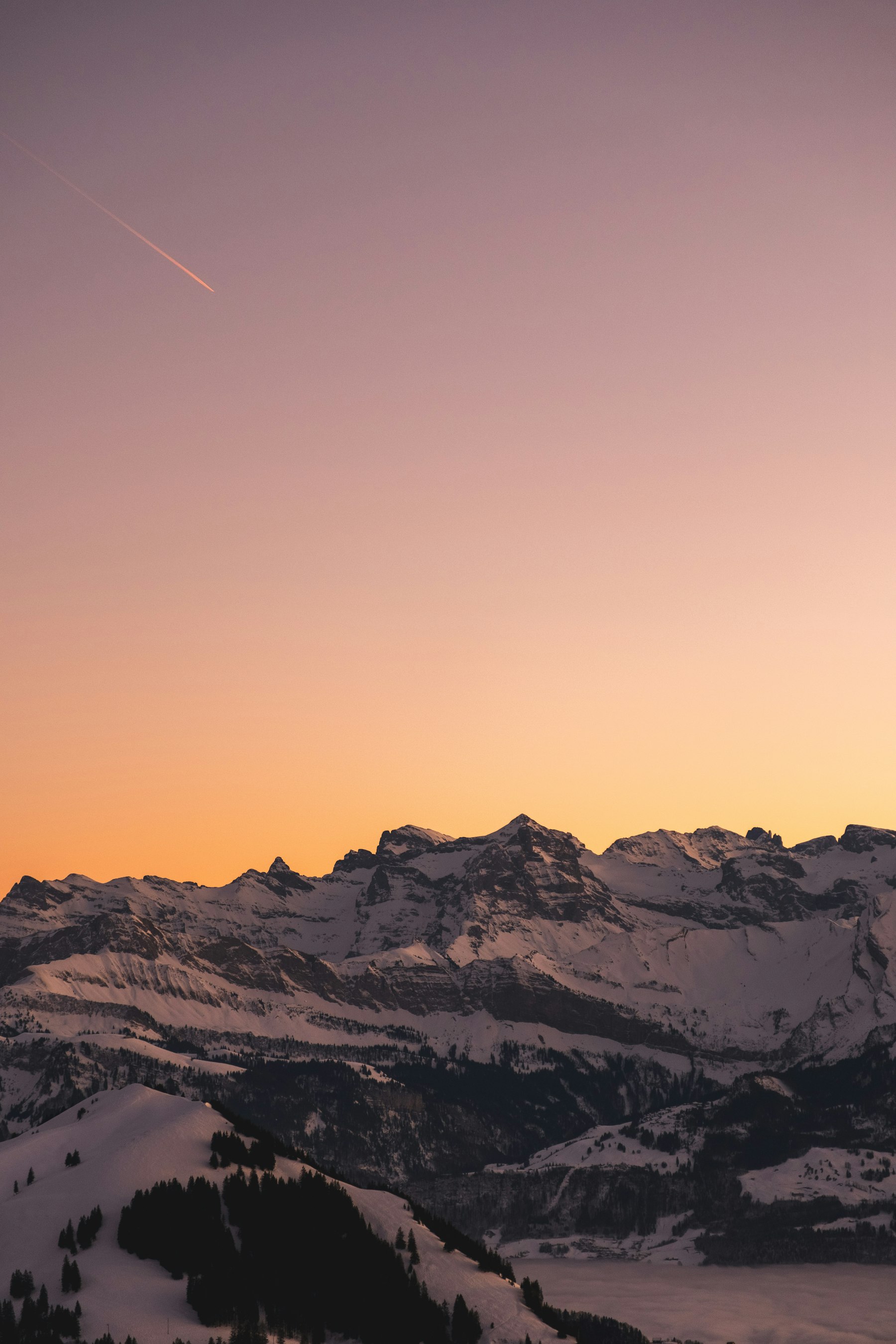 A pink and orange sunset over a snowy ridge with village lights below