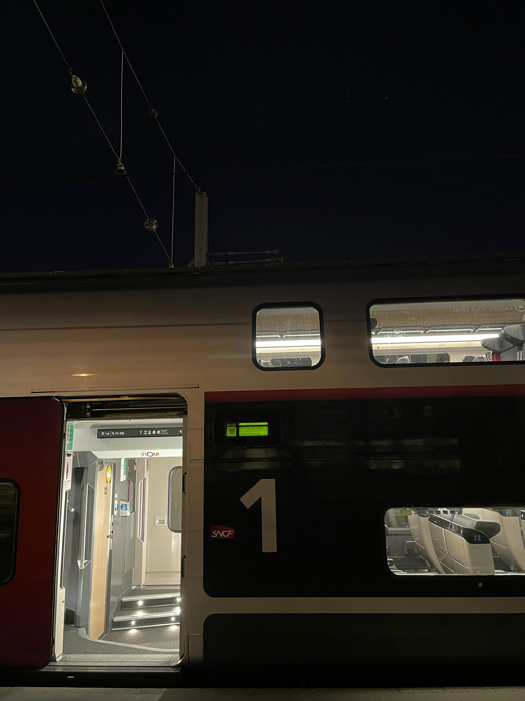 A sleeper train waiting at a dark platform at night, doors open, warm light inside
