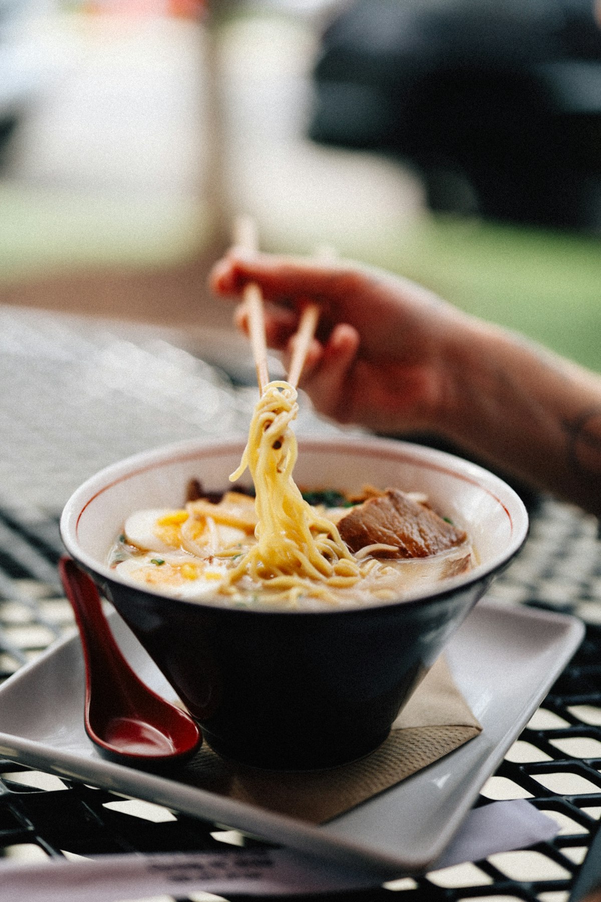 A hand pulling noodles from a bowl with chopsticks