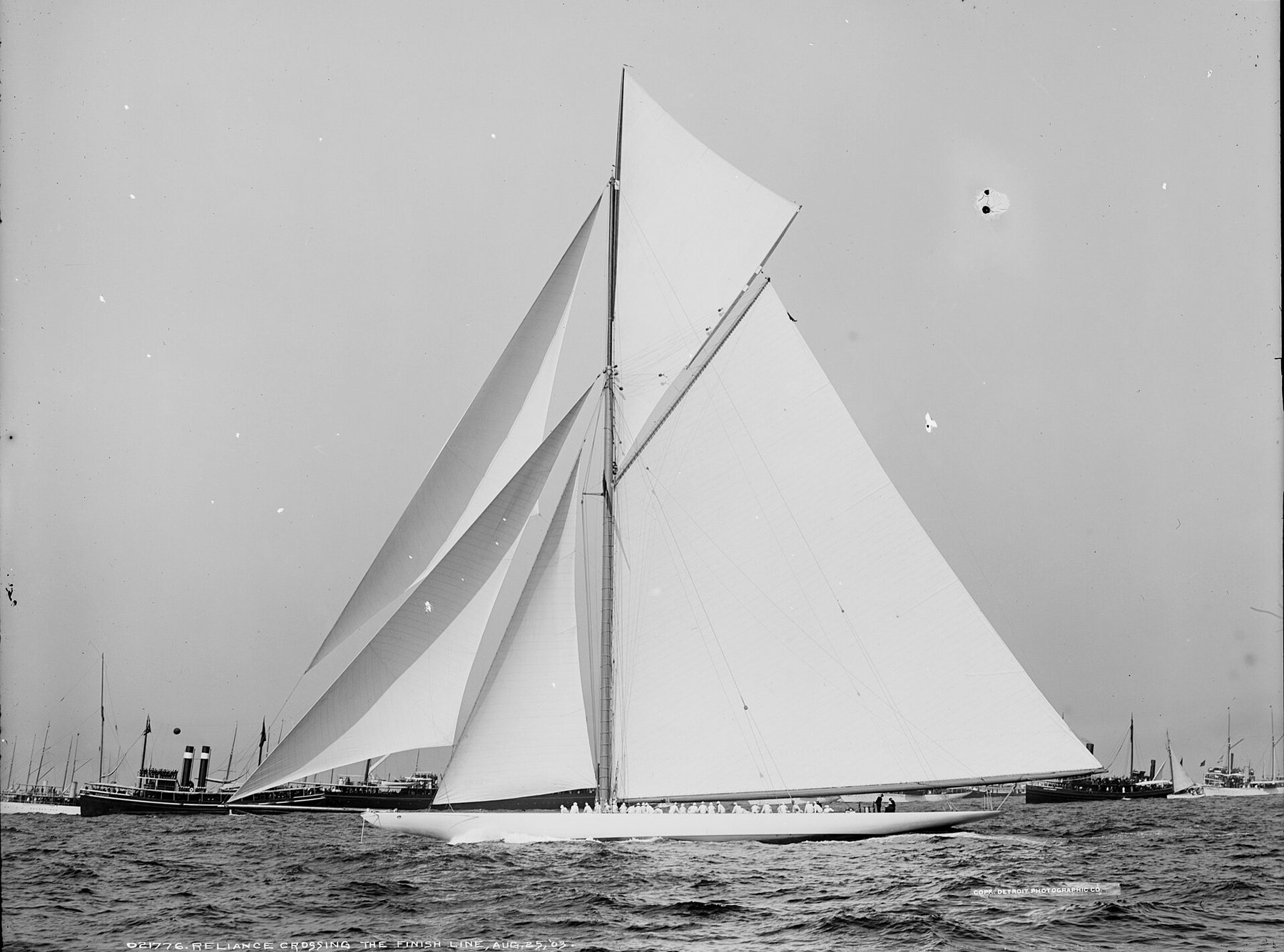 The racing yacht Reliance crossing the finish line under a mountain of white canvas, black and white photograph, 1903